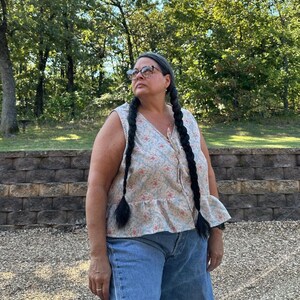 May include: A sleeveless top with a floral pattern in light blue, pink, and beige, paired with denim shorts. The top has a ruffled hem and a button-down front. The shorts are a light wash with frayed edges.