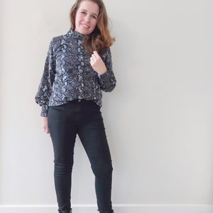 K&ouml;nnte beinhalten: Eine Frau tr&auml;gt ein schwarzes und wei&szlig;es Schlangenmuster-Rollkragen-Oberteil mit schwarzer Skinny Jeans und schwarzen Ankle Boots.