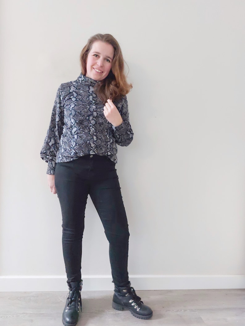 K&ouml;nnte beinhalten: Eine Frau tr&auml;gt ein schwarzes und wei&szlig;es Schlangenmuster-Rollkragen-Oberteil mit schwarzer Skinny Jeans und schwarzen Ankle Boots.