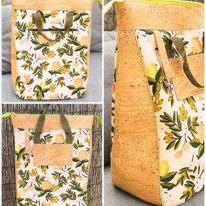 May include: A large, cork and fabric tote bag with a floral pattern. The bag has a zipped pocket on the front and a large main compartment. The bag is made of a natural cork material and has a green and white floral pattern.