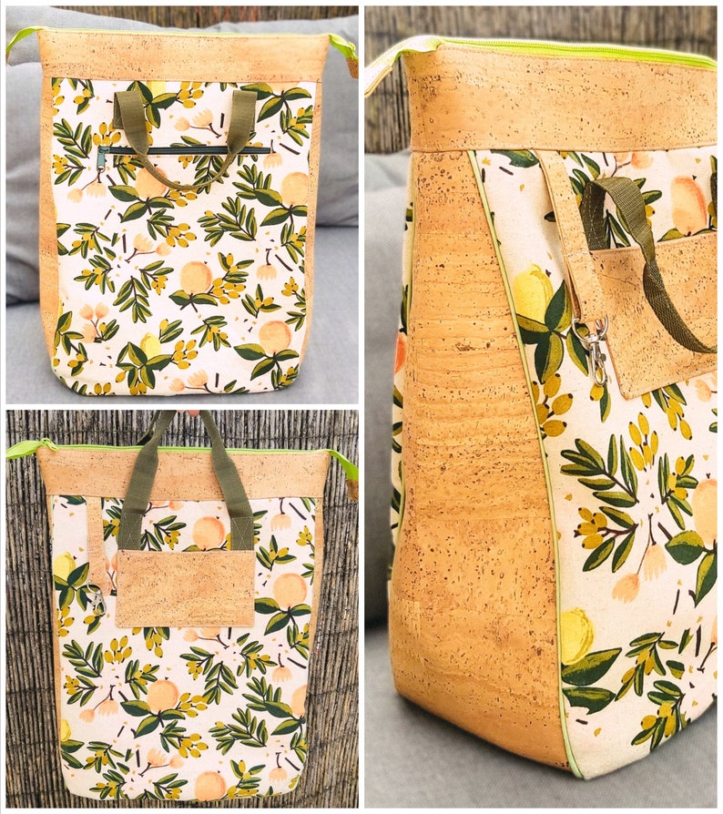 May include: A large, cork and fabric tote bag with a floral pattern. The bag has a zipped pocket on the front and a large main compartment. The bag is made of a natural cork material and has a green and white floral pattern.