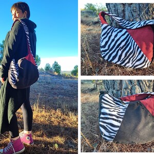 Puede incluir: Bolso de hombro con estampado de cebra, dise&ntilde;o de bloques de color rojo y negro. El bolso tiene una correa larga y una forma redondeada. El bolso se lleva al hombro. El fondo es un entorno natural al aire libre.