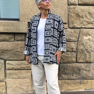 Pu&ograve; includere: Una donna indossa una giacca a motivi blu scuro e bianchi con una maglietta bianca e pantaloni beige.