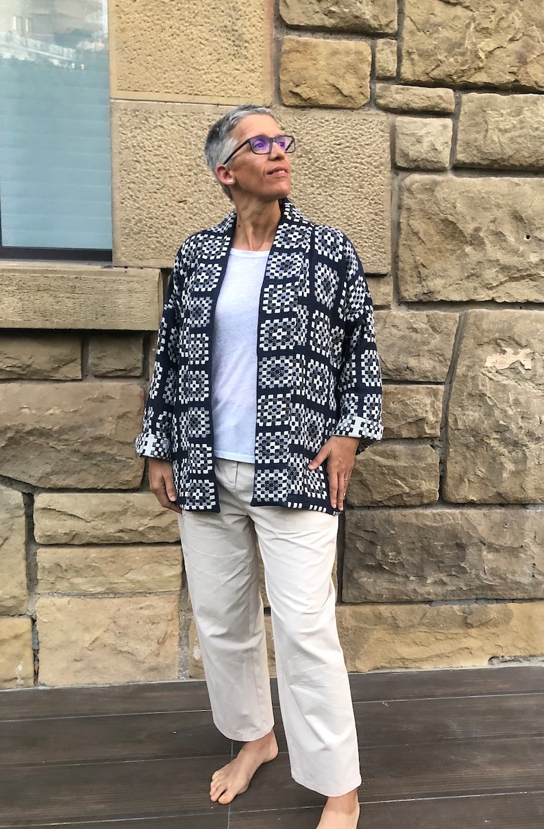 Pu&ograve; includere: Una donna indossa una giacca a motivi blu scuro e bianchi con una maglietta bianca e pantaloni beige.