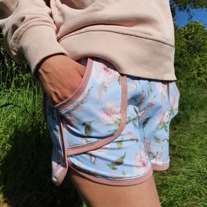 May include: Blue and pink floral print shorts with a pink trim. The shorts have a side pocket.