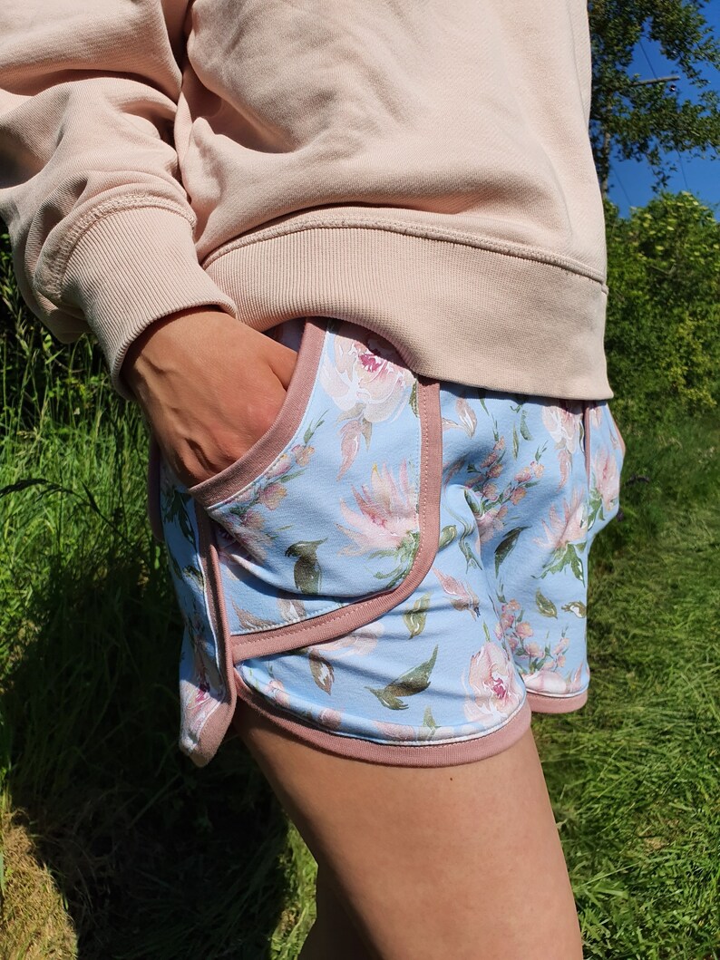 May include: Blue and pink floral print shorts with a pink trim. The shorts have a side pocket.