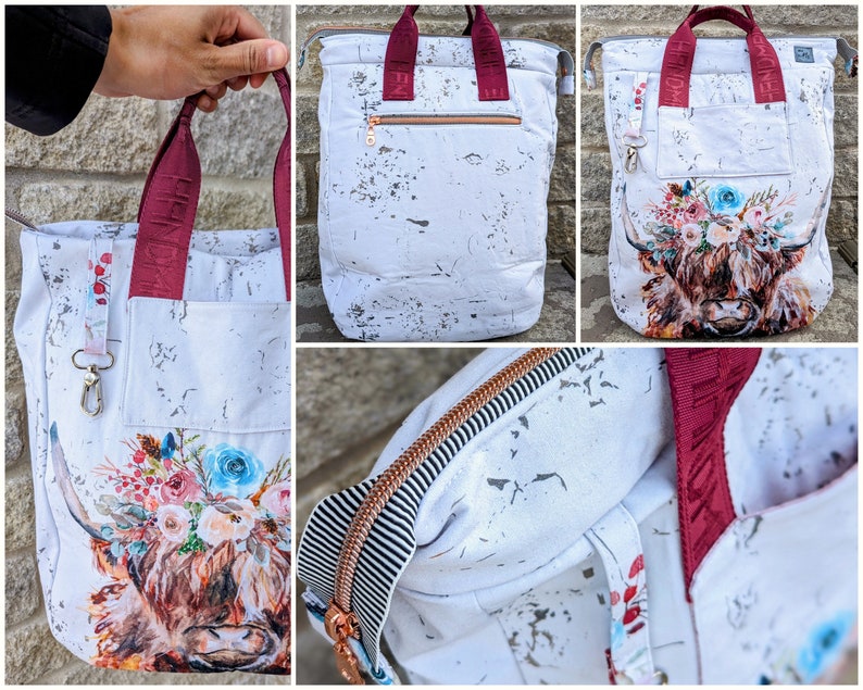 May include: White canvas tote bag with a watercolour highland cow design and floral accents. The bag has burgundy straps and a zipped pocket on the front. The bag is shown in three different views.