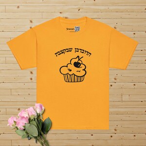 May include: A yellow t-shirt with a black cupcake graphic and the Hebrew text "Haderech Shelachsa" which translates to "The Way She Went".