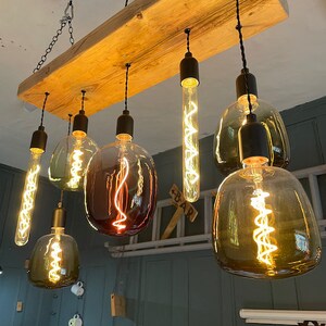 Może przedstawiać: Rustykalny drewniany żyrandol z sześcioma żar&oacute;wkami Edison. Żar&oacute;wki mają r&oacute;żne kształty i rozmiary, w tym okrągłe, owalne i długie, cienkie żar&oacute;wki. Wszystkie żar&oacute;wki są włączone i świecą, dając ciepłe, przytulne światło.