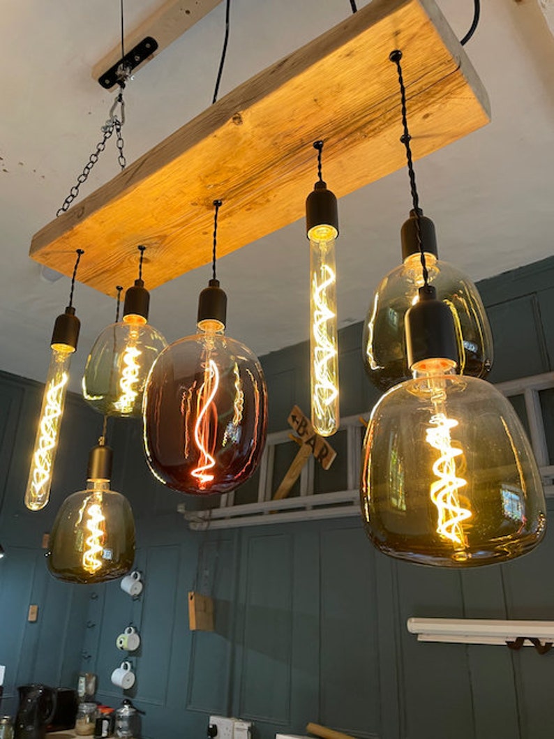 Może przedstawiać: Rustykalny drewniany żyrandol z sześcioma żar&oacute;wkami Edison. Żar&oacute;wki mają r&oacute;żne kształty i rozmiary, w tym okrągłe, owalne i długie, cienkie żar&oacute;wki. Wszystkie żar&oacute;wki są włączone i świecą, dając ciepłe, przytulne światło.