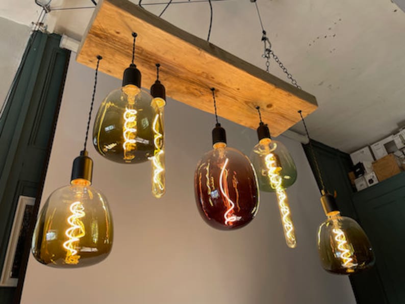 Może przedstawiać: Rustykalna drewniana lampa sufitowa z sześcioma wiszącymi żar&oacute;wkami. Żar&oacute;wki są wykonane z przezroczystego szkła z filamentem i mają r&oacute;żne kolory szkła, w tym bursztynowy, czerwony i zielony.