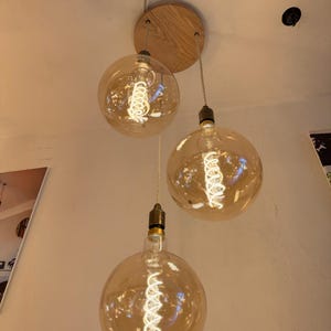 May include: Three clear glass globe light bulbs with a spiral filament hanging from a wooden ceiling fixture.