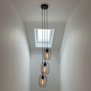 May include: A three-light pendant light fixture with black metal cage shades and warm white bulbs hanging from a white ceiling.