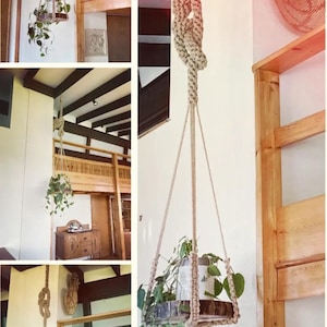 Pode incluir: Um suporte de plantas em macramé com base de madeira, suspenso por uma corda com nós. O suporte de plantas contém uma planta em vaso com folhas verdes. O fundo inclui vigas de madeira e uma parede de cor clara, criando uma estética natural e boêmia.