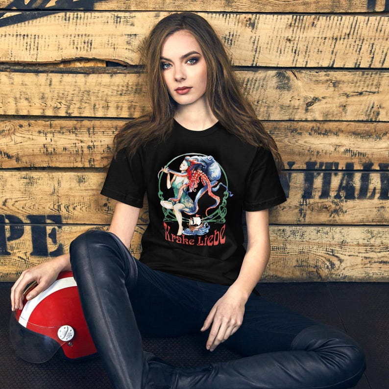 May include: Black t-shirt featuring a colorful graphic of a woman and an octopus with the text "Krake Liebe". The design includes shades of red, blue, and green. The shirt is a crew neck style.