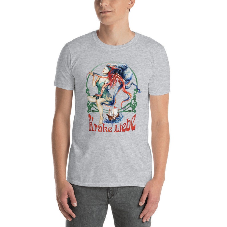 May include: A light gray t-shirt featuring a colorful illustration. The graphic depicts a woman with an octopus, a ship, and the text "Krake Liebe" in red. The design is framed by a green Celtic knot.