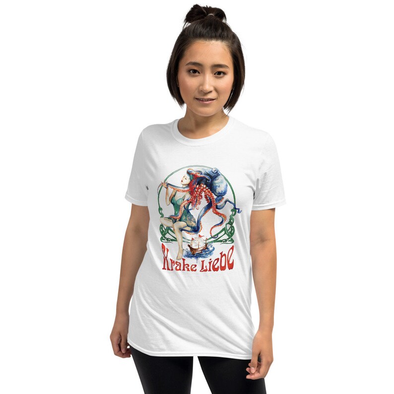 May include: White t-shirt featuring a colorful illustration of a woman with red hair and an octopus. The design includes the text "Krake Liebe" in red script, surrounded by a green and white decorative border. The shirt is a short-sleeved style.