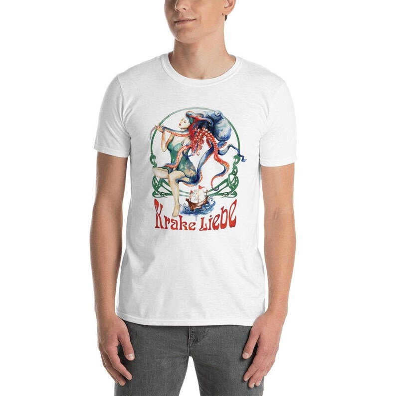 May include: White t-shirt featuring a colorful illustration of a woman, an octopus, and a ship. The design includes the text "Krake Liebe" in red and green. The artwork is set within a green circular frame.