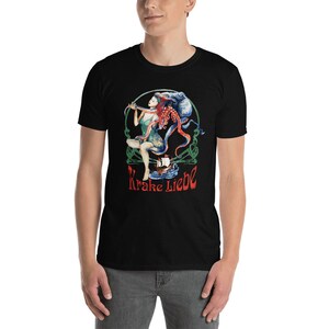 May include: Black t-shirt featuring a colorful graphic of a woman, an octopus, and a ship. The design includes the text "Krake Liebe" in red. The artwork is set within a green Celtic-style border.