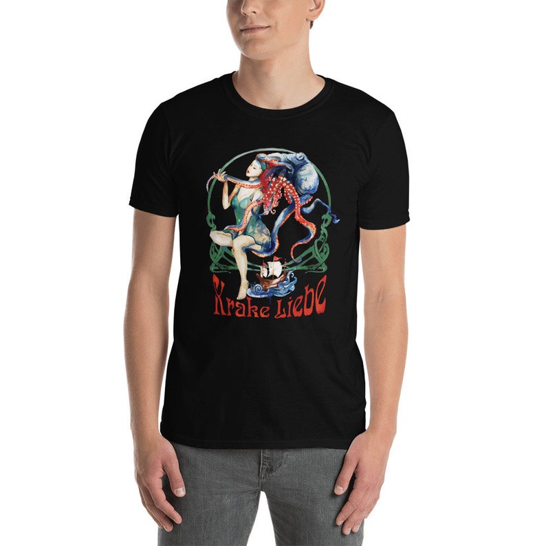May include: Black t-shirt featuring a colorful graphic of a woman, an octopus, and a ship. The design includes the text "Krake Liebe" in red. The artwork is set within a green Celtic-style border.