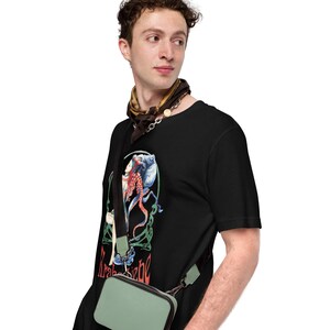 May include: Black t-shirt featuring a Kraken graphic with red and blue tentacles, and the text "Kraken bebe". The shirt is worn with a small, light green crossbody bag and a patterned scarf.