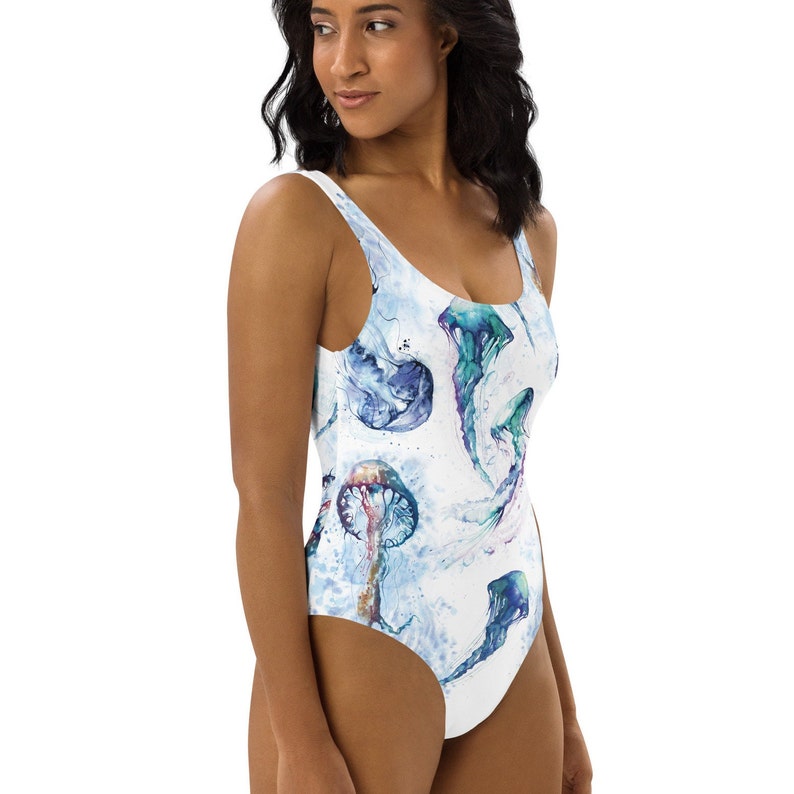 Op de afbeelding: Een wit badpak met een aquarelprint van kwallen in tinten blauw, groen en paars.