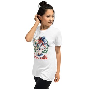 May include: White t-shirt featuring a colorful illustration of a woman, an octopus, and a small boat. The artwork includes red, blue, green, and white elements, with the text "Drake Liebe" in red and white. The shirt is made of a soft material.