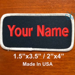 May include: A black rectangular patch with white stitching around the edges. The text "Your Name" is embroidered in red. The patch is 1.5 inches by 3.5 inches or 2 inches by 4 inches. The text "Made in USA" is printed below the patch.
