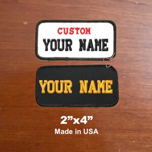 May include: Two iron-on patches, one white with red "CUSTOM" and black "YOUR NAME" text, and one black with gold "YOUR NAME" text. Both patches are 2 inches by 4 inches and say "Made in USA" below.