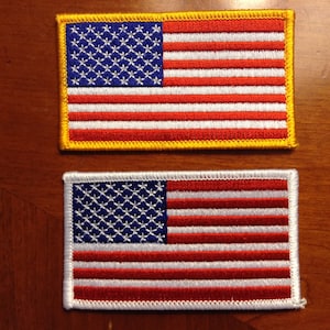 May include: Two embroidered American flag patches. The top patch has a yellow border and the bottom patch has a white border.