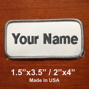 May include: White rectangular patch with gray stitching around the edges. The text "Your Name" is embroidered in black on the patch. The patch measures 1.5 inches by 3.5 inches or 2 inches by 4 inches. Made in the USA.