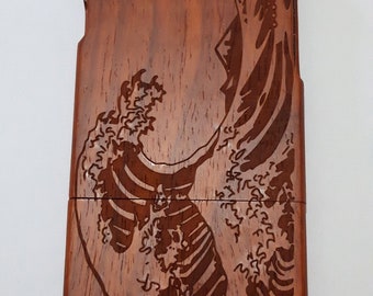 May include: A wooden phone case with a detailed carving of a wave. The case is a rich reddish-brown color.