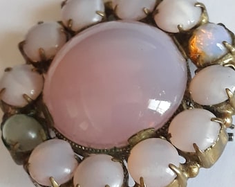 May include: A vintage brooch with a large pink glass center surrounded by smaller pink glass stones set in a gold tone metal.