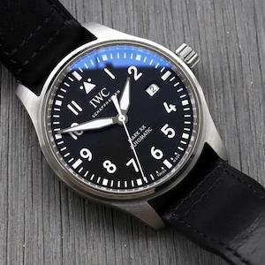 May include: An IWC Schaffhausen Mark XX Automatic wristwatch with a round stainless steel case, a black dial featuring white Arabic numerals, luminous hands, a date window at the three o'clock position, and a black leather strap.