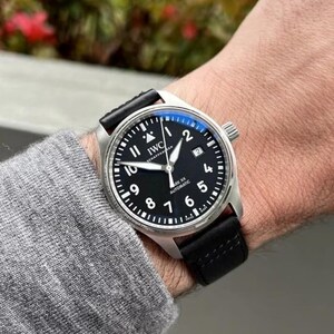 May include: An IWC Mark XX automatic wristwatch with a round stainless steel case, a black dial featuring white Arabic numerals, a date window at the three o'clock position, and a black leather strap with visible stitching.