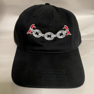 May include: Black baseball cap with a curved brim. The cap features an embroidered design of a chain with red and white accents. The cap is made of a durable fabric and has an adjustable strap for a comfortable fit.