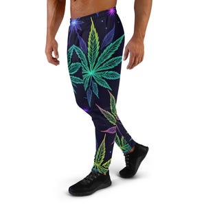 Puede incluir: Pantalones de chándal negros con un estampado de hojas de marihuana de colores. Las hojas están delineadas en verde neón, rosa y azul.