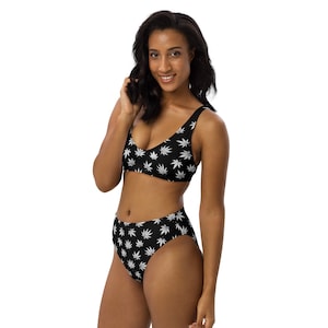 May include: Black bikini with a white marijuana leaf pattern. The bikini top has a scoop neck and adjustable straps. The bikini bottom is high-waisted.