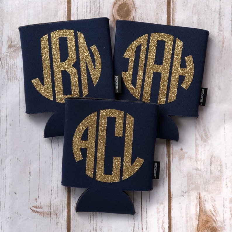 May include: Three navy blue can coolers with gold glitter monogram initials. The initials are JBM, JAH, and ACL.
