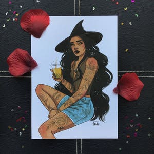 May include: A witch with long black hair and a black witch hat is sitting with her legs crossed. She is wearing a black tank top with a floral design, blue denim shorts, and has tattoos on her arms and legs. She is holding a clear plastic cup with a yellow drink. The background is white.