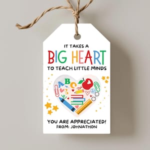 Puede incluir: Una etiqueta de regalo blanca con una cuerda marrón. La etiqueta tiene el texto "IT TAKES A BIG HEART TO TEACH LITTLE MINDS" en letras coloridas. Un gráfico en forma de corazón incluye ilustraciones escolares. El texto "YOU ARE APPRECIATED! FROM: JOHNATHON" está en la parte inferior.
