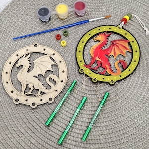 May include: A craft kit with two dragon ornaments, one unpainted and one painted red and orange. The kit includes paint pots, a paintbrush, beads, and green metal tubes. The ornaments are circular with star details.