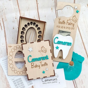 May include: A wooden tooth fairy door with a slot for a tooth and money. The door has the text "Tooth Fairy Pick up & Drop Off" and a small fairy illustration. A white tooth with the name "Cameron" is attached to the door. A wooden box with a compartment for each tooth and a small journal with the text "Cameron's Baby Teeth Journal" are also included.