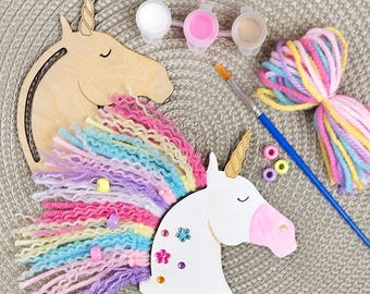 May include: A craft kit for making a unicorn head with a wooden base, white paint, pink paint, beige paint, a paintbrush, colorful yarn, and decorative gems.