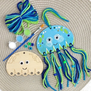 May include: A DIY craft kit featuring two jellyfish-shaped wooden cutouts, one painted blue with googly eyes and yarn tentacles, the other plain wood. Includes a paintbrush, three small paint pots, a bundle of blue and green yarn, and beads.