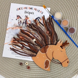 May include: A horse macrame paint kit featuring a painted wooden horse head, yarn mane, and paint pots. The kit includes a paintbrush and a printed sheet with horse illustrations. The horse head is light brown with darker brown markings.