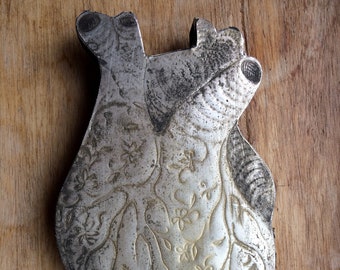 May include: A silver heart-shaped ornament with a detailed floral design. The ornament is slightly tarnished and has a rustic look.