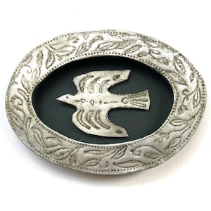 Puede incluir: Hebilla de cinturón ovalada de metal plateado con un borde floral en relieve. El centro presenta un fondo negro con una paloma plateada en vuelo. La hebilla probablemente está hecha de una aleación de metal y es adecuada para un cinturón.