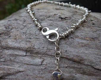 May include: A silver bracelet with a silver clasp and a small silver charm with a gold heart. The bracelet is made of small silver beads.