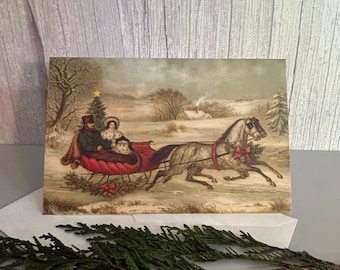May include: A rectangular greeting card featuring a vintage-style illustration of two people riding in a red horse-drawn sleigh through a snowy landscape. The scene includes two grey horses, a decorated Christmas tree, and a small house.